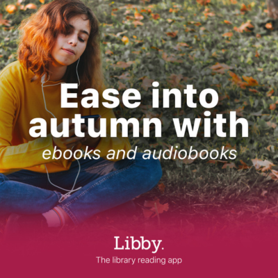 A young person with wavy, shoulder-length auburn hair sits cross-legged on grass scattered with autumn leaves. They are wearing a yellow sweater and blue jeans, listening to something on white earphones while holding a smartphone. Large white text in the center reads: “Ease into autumn with ebooks and audiobooks.” At the bottom, against a plum gradient background, the Libby logo appears in white with the tagline: “The library reading app.”